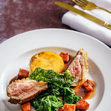 Elegantes Gericht mit rosa gebratenem Fleisch, Blattgemüse, Kartoffel und Würfeln