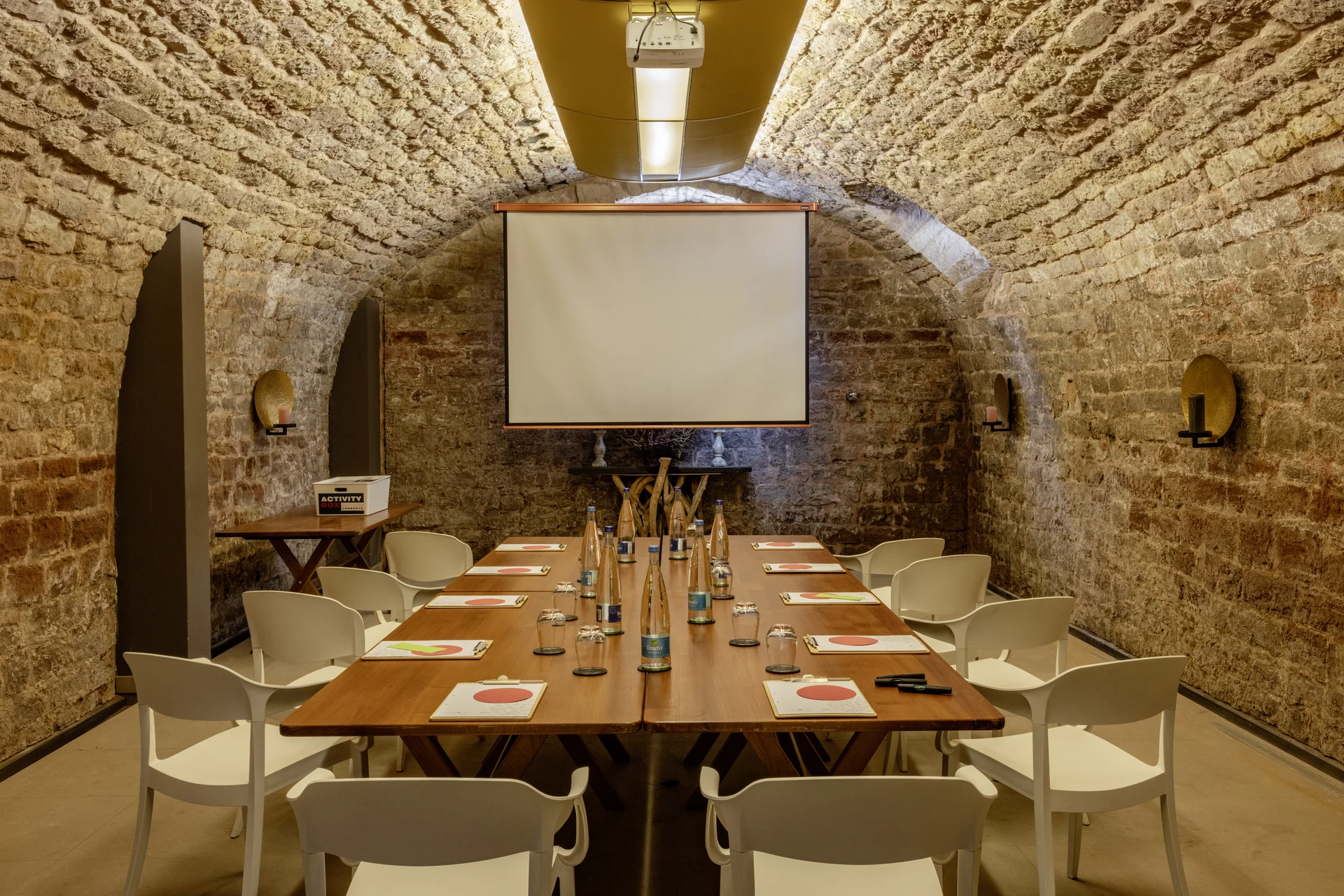 Konferenzraum mit Steintunneldecke, Holztisch, weißen Stühlen und Projektionsleinwand