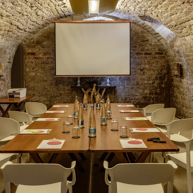 Konferenzraum mit Steintunneldecke, Holztisch, weißen Stühlen und Projektionsleinwand