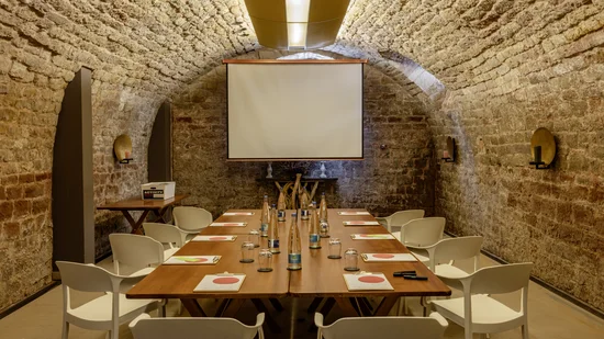 Konferenzraum mit Steintunneldecke, Holztisch, weißen Stühlen und Projektionsleinwand