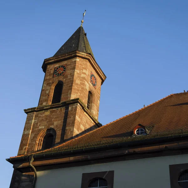 Kirchturm aus Stein mit Uhr und spitzem Dach bei klarem Himmel