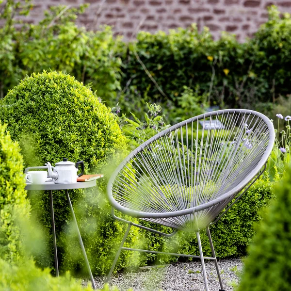 Runder Stuhl und Tisch mit Teekanne in grünem Garten mit Buch
