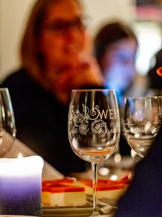Gläser und Kerze auf einem Tisch bei einem Abendessen mit unscharfen Personen im Hintergrund