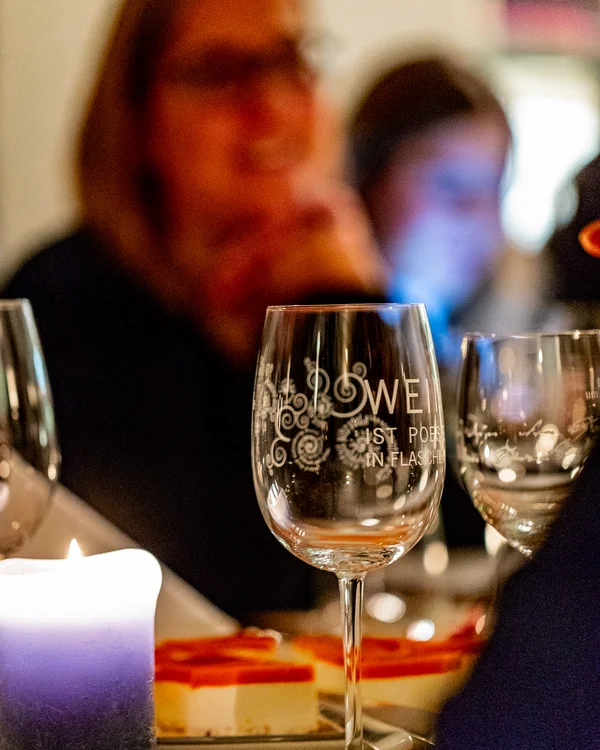Gläser und Kerze auf einem Tisch bei einem Abendessen mit unscharfen Personen im Hintergrund