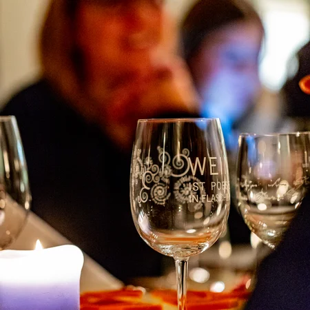 Gläser und Kerze auf einem Tisch bei einem Abendessen mit unscharfen Personen im Hintergrund