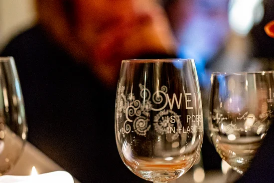 Fünf Winzer – fünf Freunde Gläser und Kerze auf einem Tisch bei einem Abendessen mit unscharfen Personen im Hintergrund