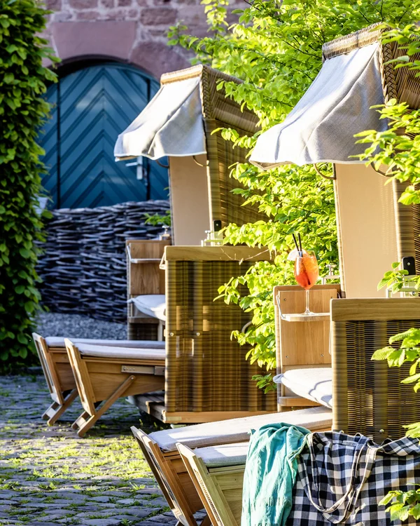 Strandkörbe mit Getränken und Tasche in sonnigem Garten mit altem Steinpflaster