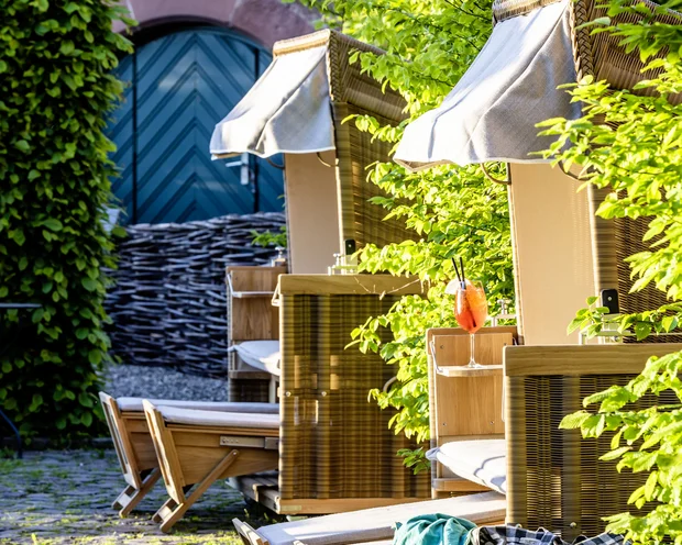 Strandkörbe mit Getränken und Tasche in sonnigem Garten mit altem Steinpflaster