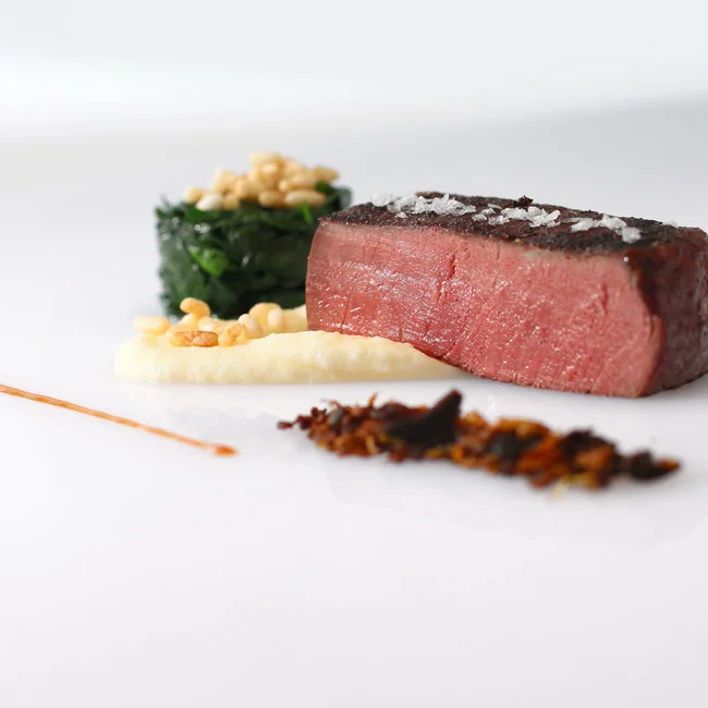 Medium gebratenes Steak mit Beilagen kunstvoll auf weißem Teller angerichtet