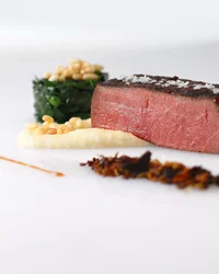 Medium gebratenes Steak mit Beilagen kunstvoll auf weißem Teller angerichtet