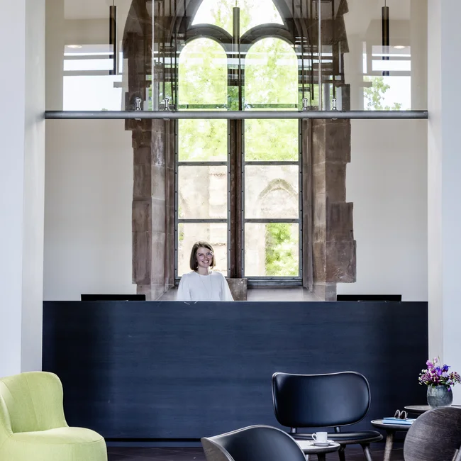 Rezeption mit lächelnder Frau und modernen Stühlen in einem Raum mit gotischem Fenster