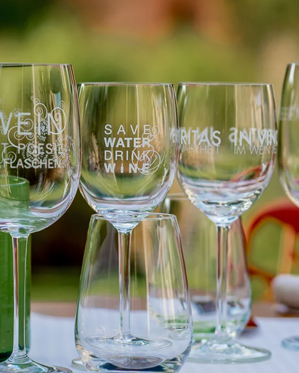 Mehrere Weingläser mit Aufdrucken stehen auf einem Tisch im Freien