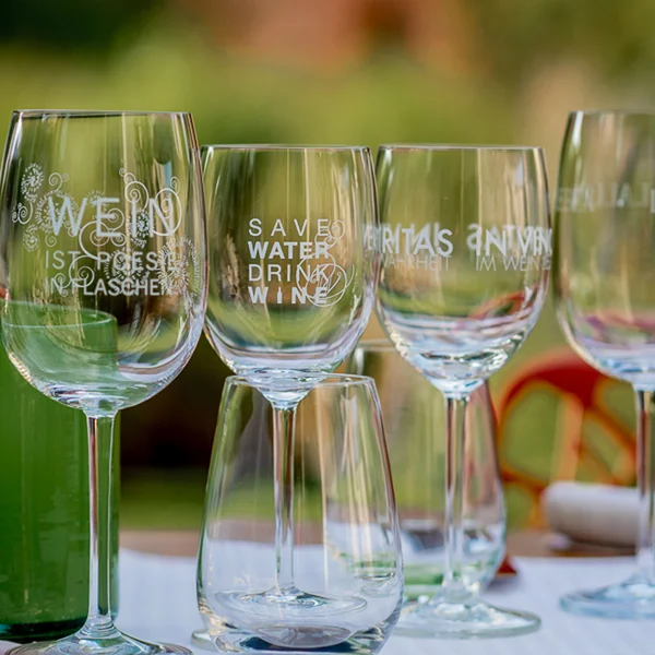 Mehrere Weingläser mit Aufdrucken stehen auf einem Tisch im Freien