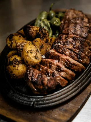 Gegrilltes Steak mit Bratkartoffeln und grünen Paprikaschoten auf einer gusseisernen Platte