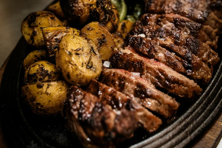 Gegrilltes Steak mit Bratkartoffeln und grünen Paprikaschoten auf einer gusseisernen Platte