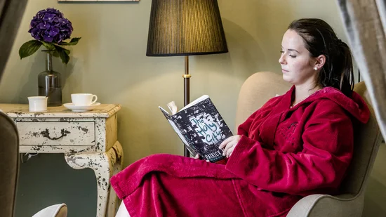 Frau in rotem Bademantel liest in einem Sessel in gemütlichem Zimmer