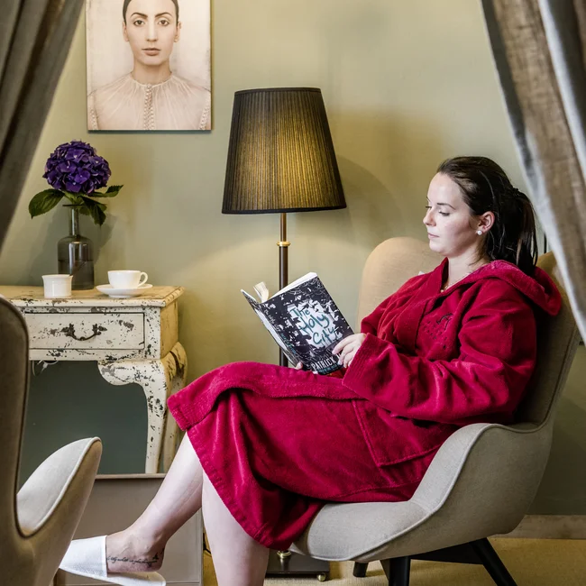 Frau in rotem Bademantel liest in einem Sessel in gemütlichem Zimmer
