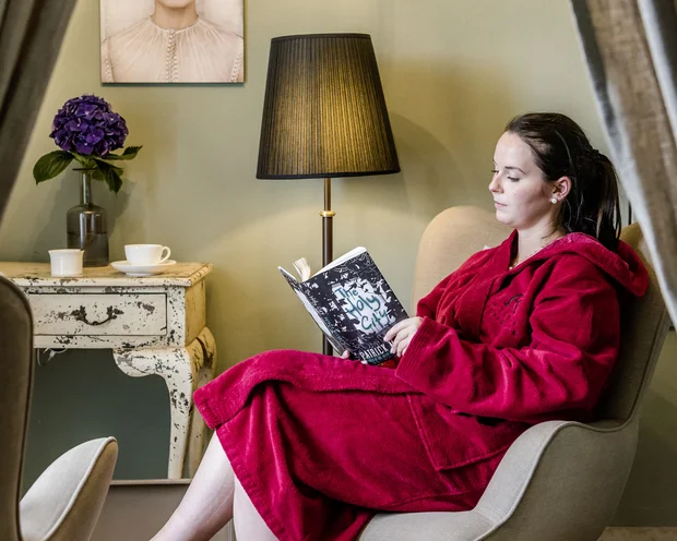 Frau in rotem Bademantel liest in einem Sessel in gemütlichem Zimmer