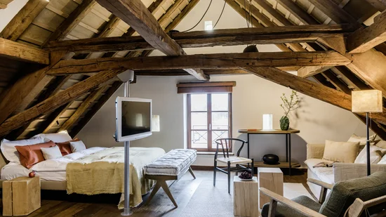 Gemütliches Dachzimmer mit Holzbalken, Bett, Sitzbereich und Fernseher