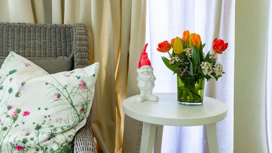 Blumenvase mit roten und gelben Tulpen neben einem Gartenzwerg auf weißem Tisch