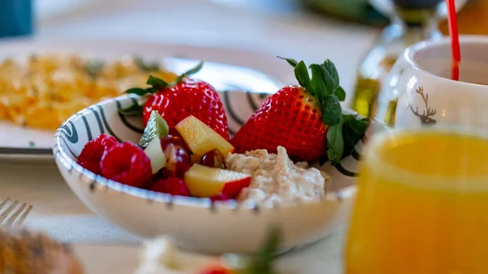 Schale mit frischen Früchten und Hüttenkäse, daneben ein Glas Orangensaft
