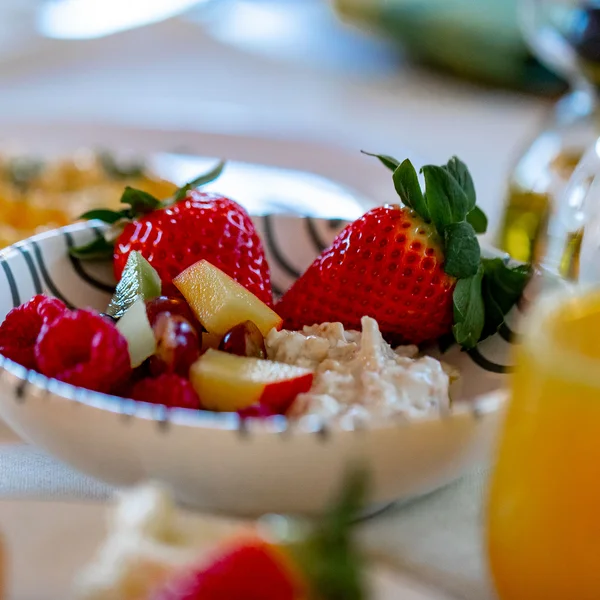 Schale mit frischen Früchten und Hüttenkäse, daneben ein Glas Orangensaft