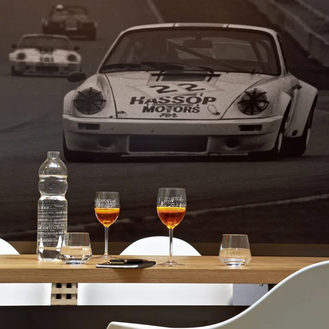 Weißes Autorennen-Auto vor Schwarz-Weiß-Rennszene an Wand hinter Tisch mit Gläsern