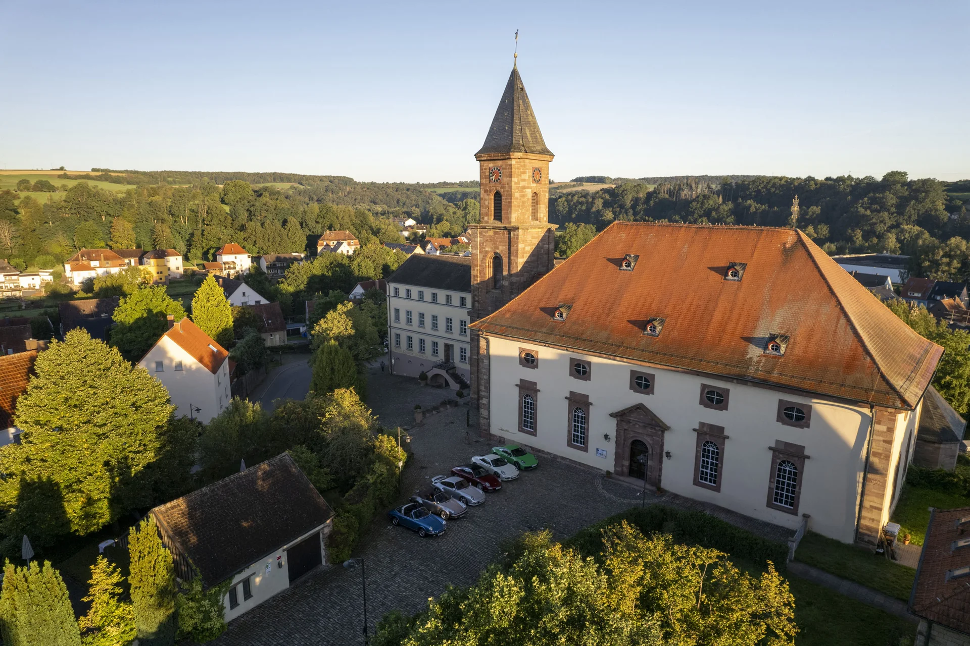 Historische Kirche mit rotem Dach und Turm in einem grünen Dorf in der Abendsonne
