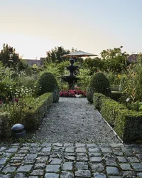 Wege und Hecken in einem Garten mit einer Brunnenanlage und Blumenbeeten