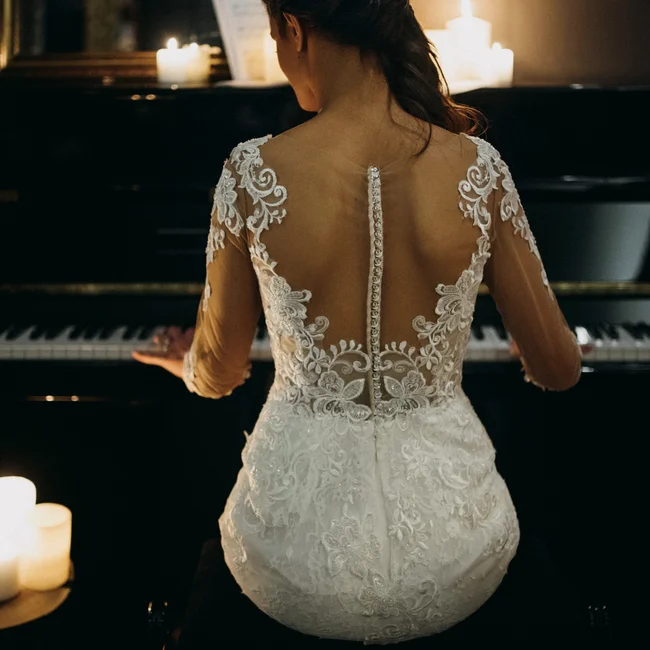Frau in Spitzen-Brautkleid spielt Klavier bei Kerzenlicht