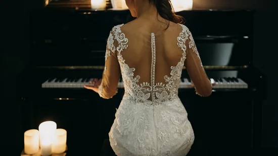 Frau in Spitzen-Brautkleid spielt Klavier bei Kerzenlicht