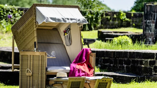 Strandkorb mit roter Decke auf grünem Rasen bei sonnigem Wetter