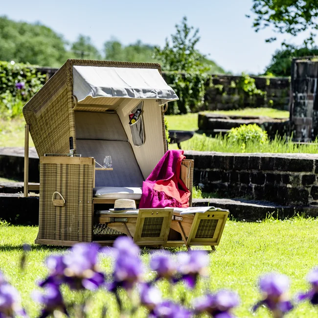 Strandkorb mit roter Decke auf grünem Rasen bei sonnigem Wetter