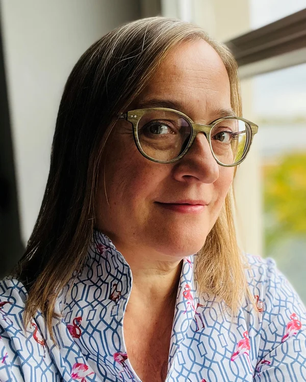 Frau mit Brille und floral gemustertem Hemd vor Fenster