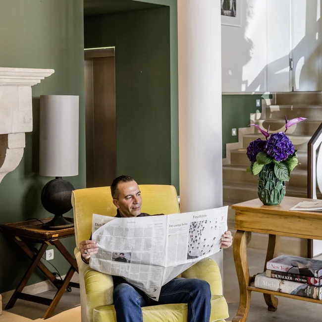 Mann liest Zeitung in gelbem Sessel in modernem Wohnzimmer