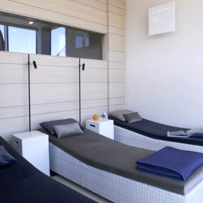 Drei moderne Liegen mit grauen Polstern und blauen Decken in einem hellen Raum