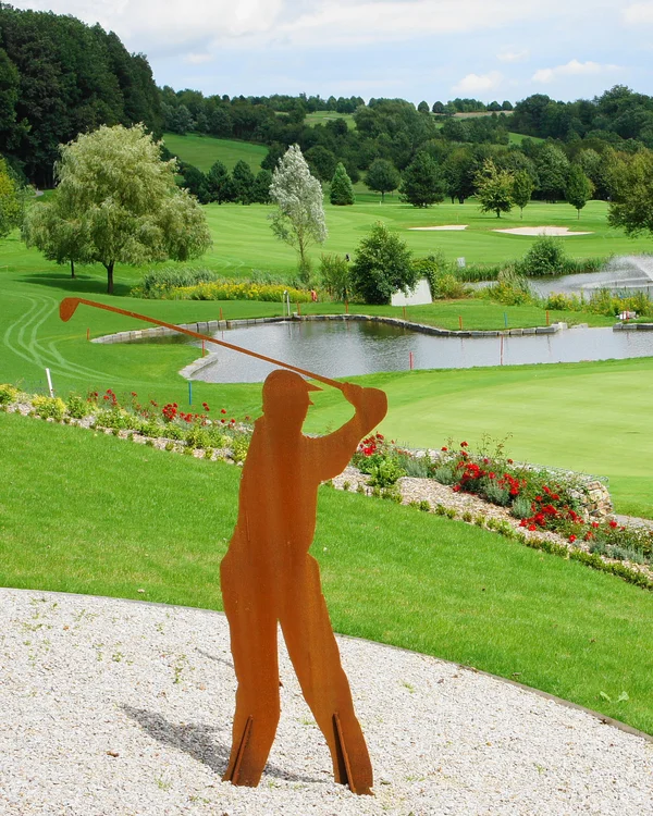Golfschläger Skulpturen auf einem gepflegten Golfplatz mit Teich und Bäumen