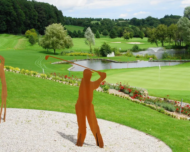 Golfschläger Skulpturen auf einem gepflegten Golfplatz mit Teich und Bäumen