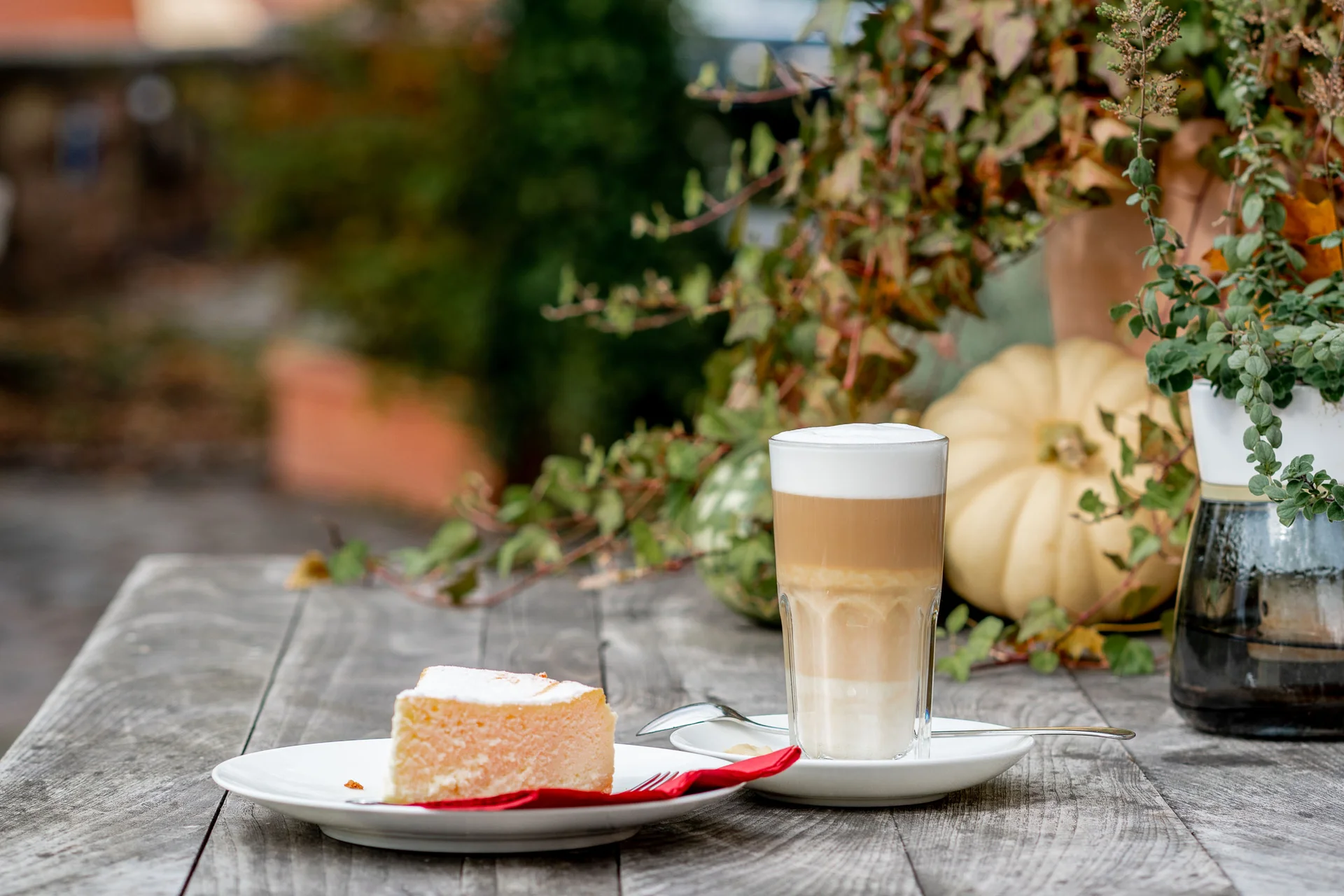 Stück Käsekuchen mit Latte auf Holztisch mit herbstlicher Dekoration