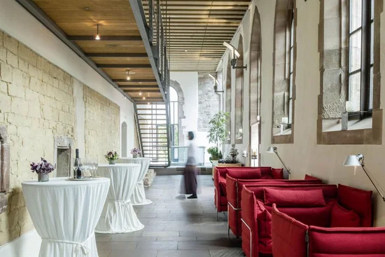 Moderne Lounge mit roten Sofas und Stehtischen in historischem Gebäude