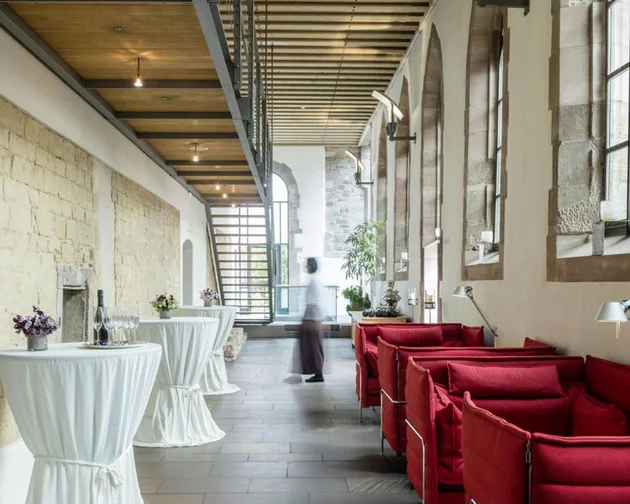 Moderne Lounge mit roten Sofas und Stehtischen in historischem Gebäude