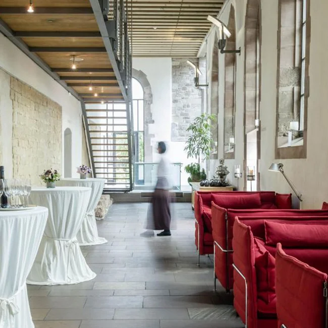 Moderne Lounge mit roten Sofas und Stehtischen in historischem Gebäude