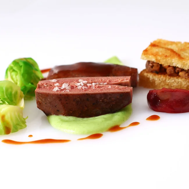 Fein angerichtetes Gourmetgericht mit Fleisch, Rosenkohl und Sauce auf weißem Teller