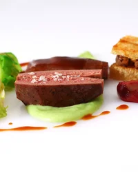 Fein angerichtetes Gourmetgericht mit Fleisch, Rosenkohl und Sauce auf weißem Teller