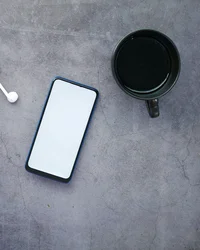 Smartphone, schwarze Kaffeetasse, Ohrhörer und Füllfederhalter auf grauem Tisch