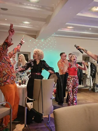 Menschen feiern und singen mit Mikrofon auf einer Party in bunten Outfits