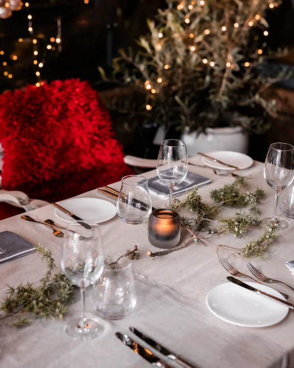 Festlich gedeckter Tisch mit Kerze, Gläsern und rotem Kissen im Hintergrund