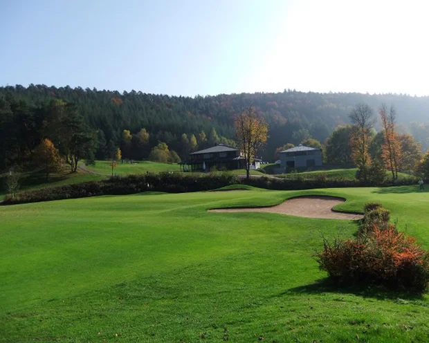 Golfplatz mit Bunker, Häusern und Wald im Hintergrund bei sonnigem Wetter