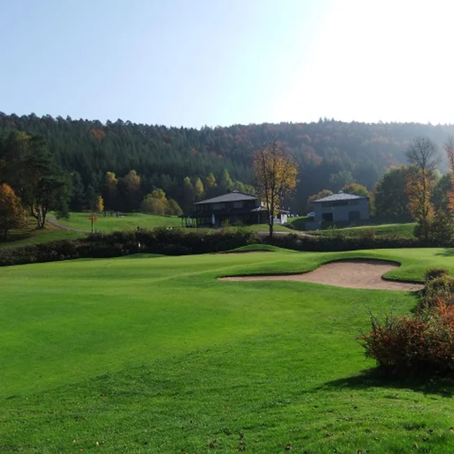 Golfplatz mit Bunker, Häusern und Wald im Hintergrund bei sonnigem Wetter