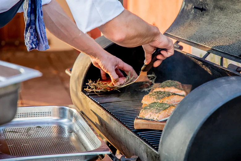 Person legt Lachsfilets mit Kräutern auf einen Grill